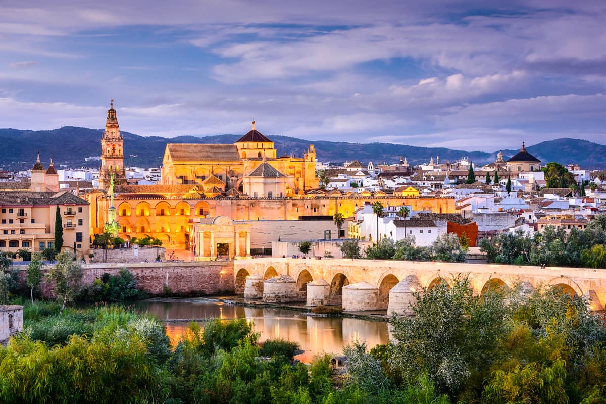 a cityscape of a medieval city with a abridge above a river at dusk and city lights on; Cordoba in Andalusia, Spain