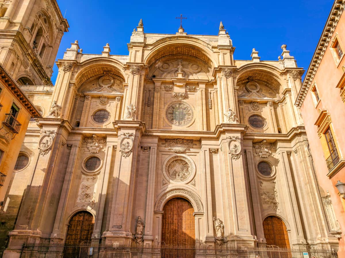 the front facade of a cathedral with light orange color, lit up by the setting sun and piece of clear deep blue sky above'; the Granada Cathedral in Andalusia, Spain